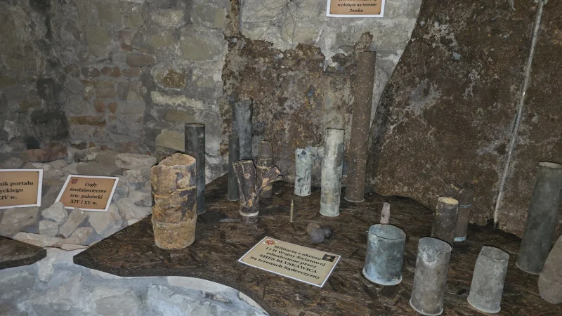 Ekspozycja historyczna przedstawiająca elementy militarne związane z okresem II wojny światowej, na tle murów baszty lub fortyfikacji.