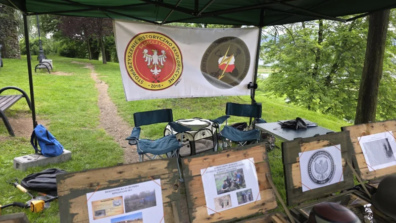 Grupa osób na terenie historycznego stowarzyszenia, podczas wydarzenia lub spotkania. W tle widać zabytkową architekturę i teren zielony.