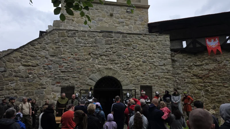 Historyczna baszta obronna w stylu militarnego kompleksu na placu miejskim. Przed nią stoi grupa ludzi obserwujących wydarzenie lub spacerując po terenie historycznym.
